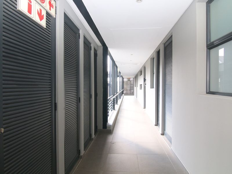A well-maintained apartment building corridor featuring tiled flooring, louvered doors, and modern recessed lighting.