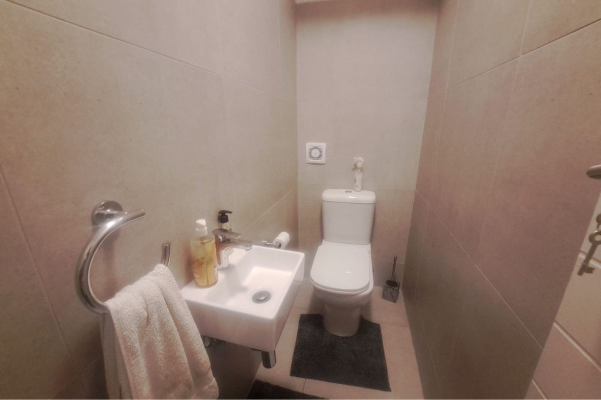 A compact guest bathroom featuring modern neutral wall tiles, a wall-mounted basin, and a standard toilet.