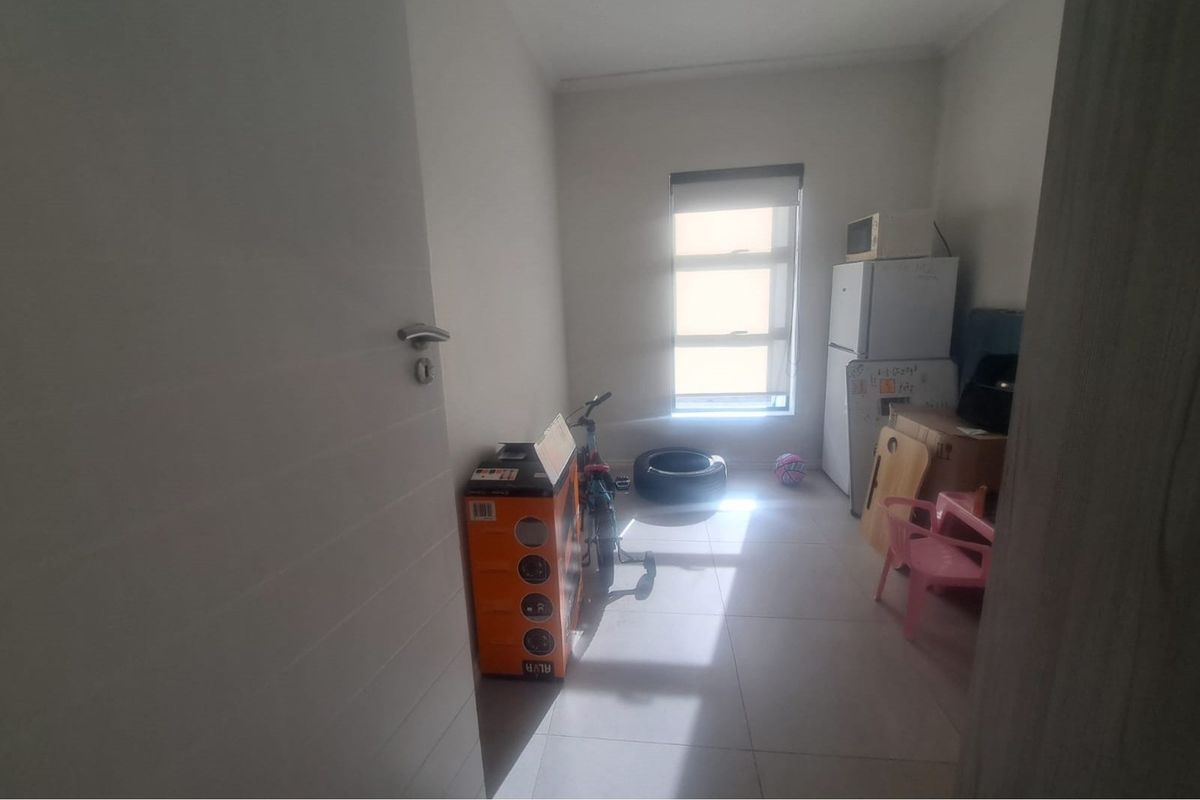 A small, neutrally painted room featuring tiled flooring and a window with a roller blind, currently used for storage.