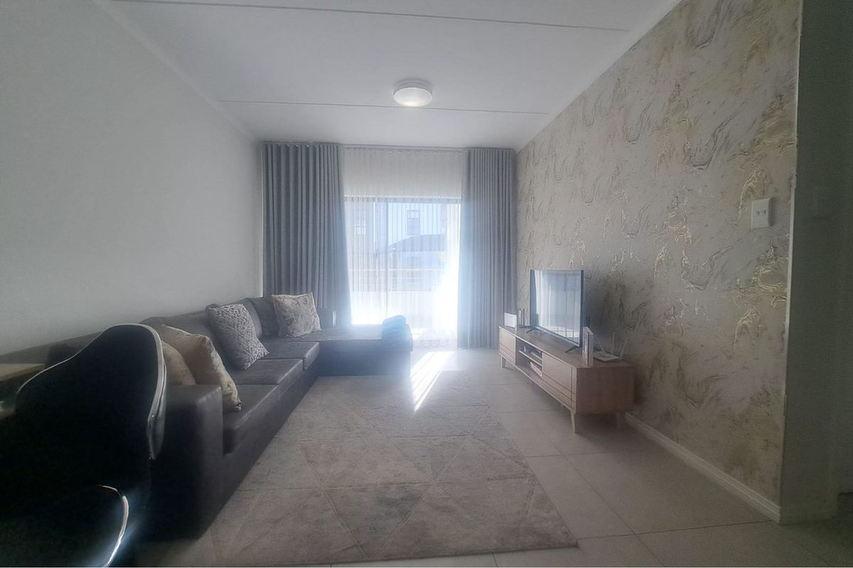A well-maintained living room featuring tiled flooring, a decorative feature wall, and a sliding glass door providing natural light.