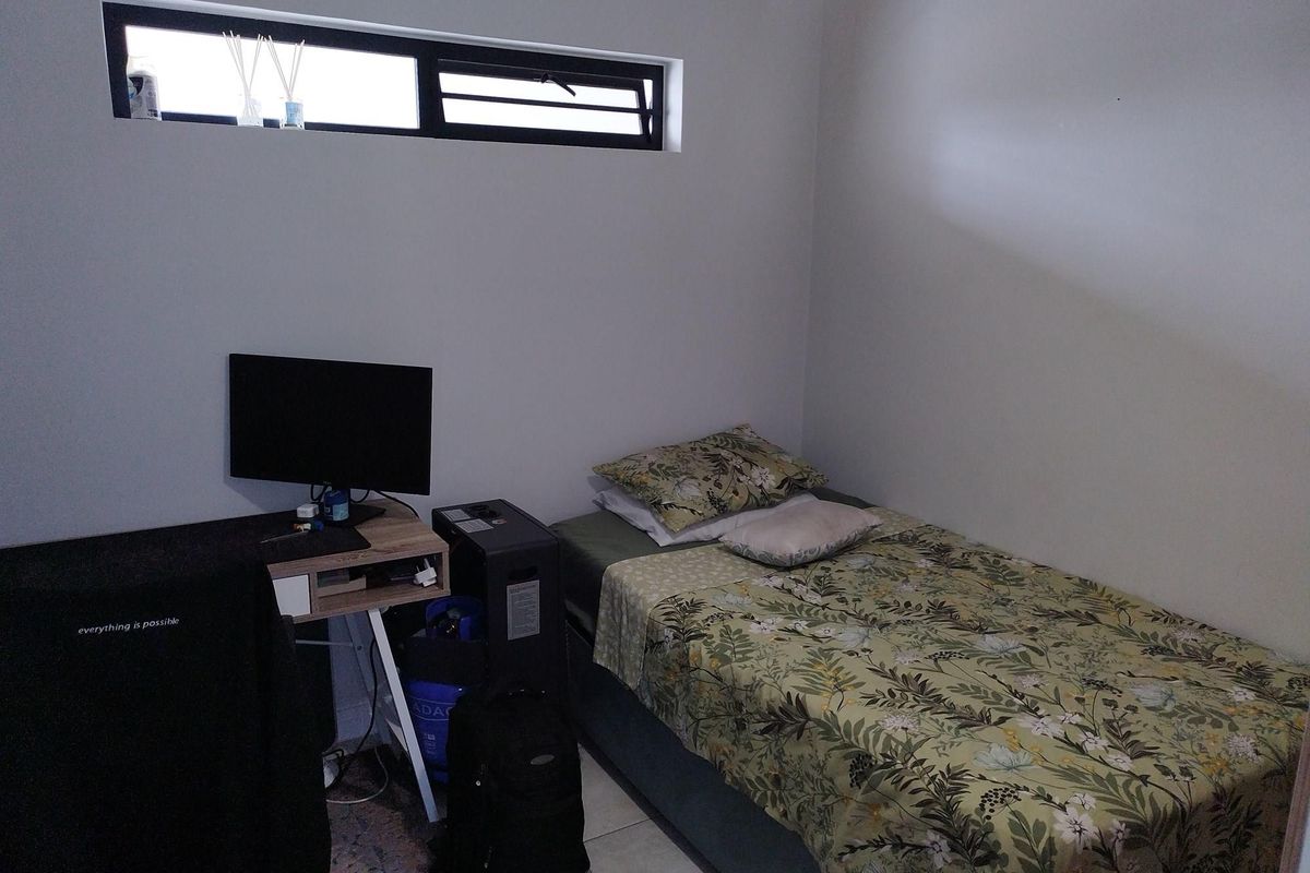A compact bedroom featuring a high-set horizontal window, neutral wall finishes, and tiled flooring.