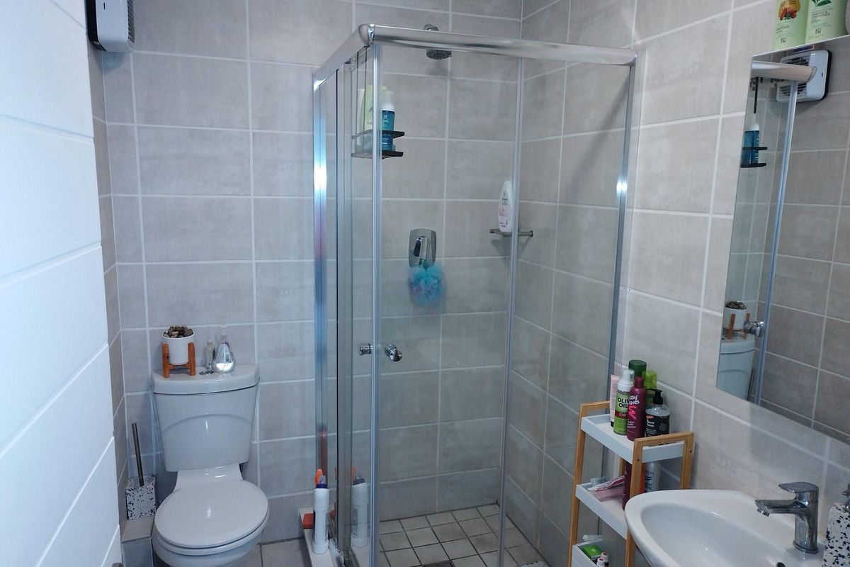 A functional bathroom featuring a glass-enclosed shower, a standard toilet, and a wall-mounted mirror above the vanity basin with neutral wall tiling.