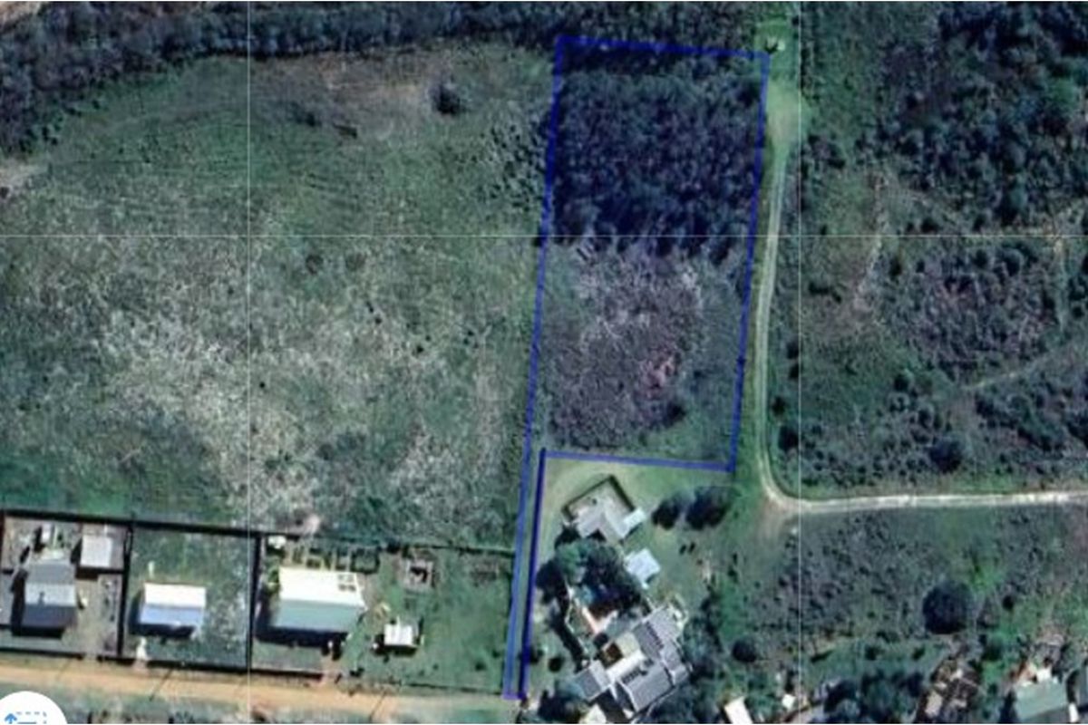 Aerial view of a vacant residential plot with boundary lines highlighted, showing surrounding vegetation and nearby residential properties.