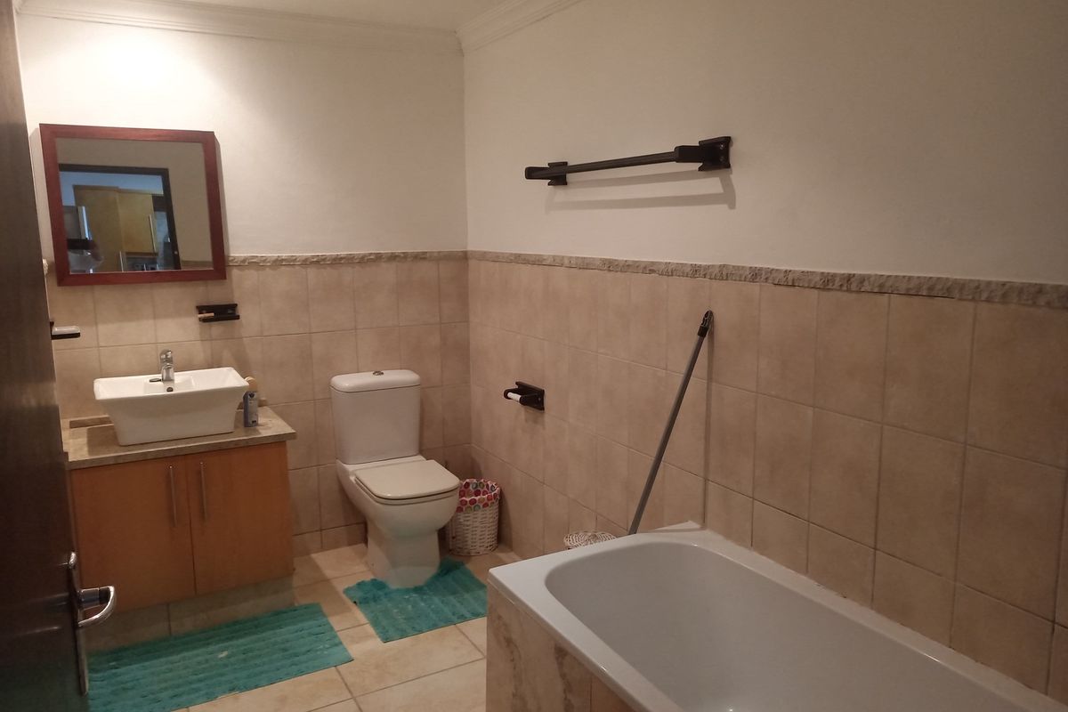 A functional bathroom featuring a built-in bathtub, a vessel sink vanity with storage, a toilet, and neutral wall tiling.