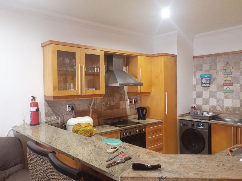 A functional kitchen featuring light wood cabinetry, granite countertops, a built-in oven with extractor fan, and an integrated washing machine.
