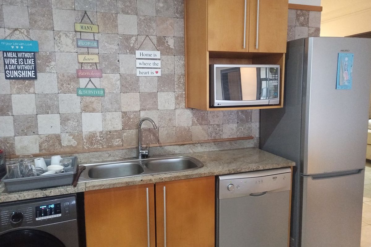 A functional kitchen area featuring wood-finish cabinetry, stone-look tiled backsplash, double stainless steel sink, and integrated space for appliances.