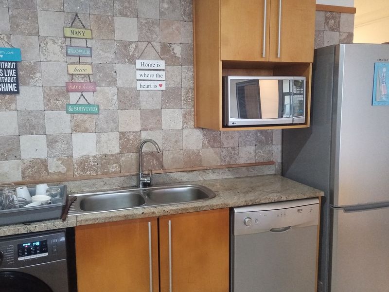 A functional kitchen area featuring wood-finish cabinetry, stone-look tiled backsplash, double stainless steel sink, and integrated space for appliances.