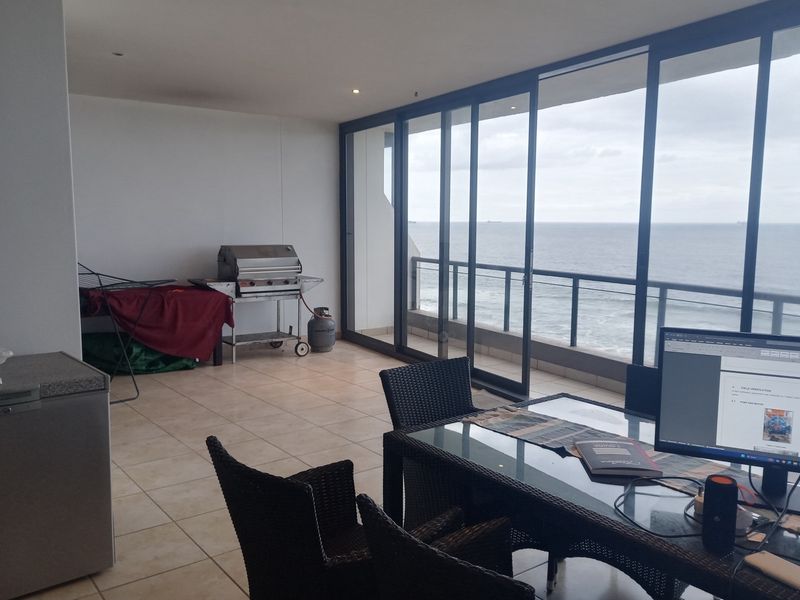 Spacious covered balcony featuring tiled flooring, large sliding glass doors, and expansive ocean views, ideal for outdoor dining and relaxation.