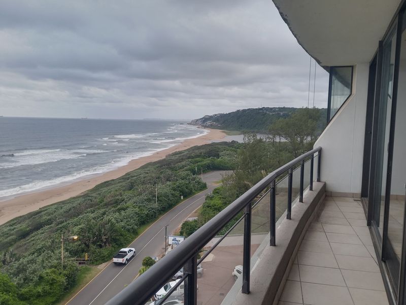 A spacious balcony offering panoramic coastal views, featuring tiled flooring and a secure metal railing overlooking the beach and coastline.
