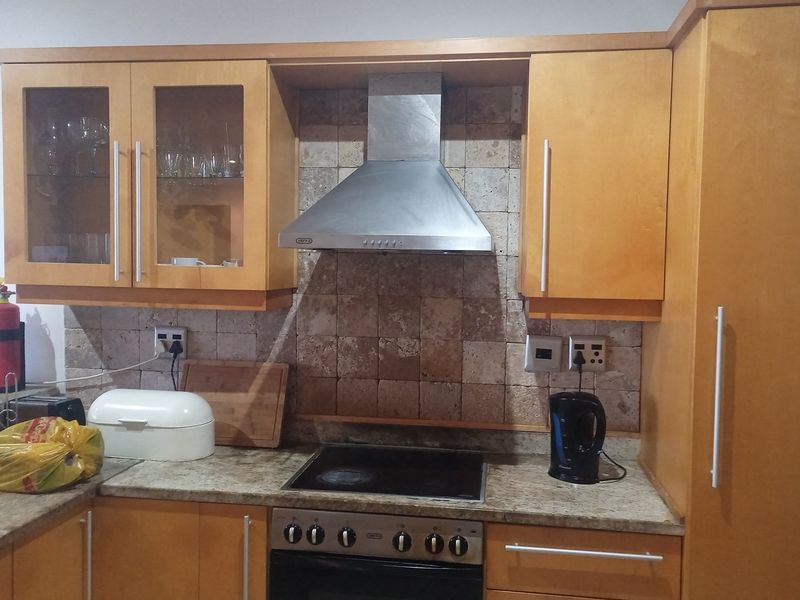 A functional kitchen featuring light wood cabinetry, stone-tiled backsplash, granite countertops, and a built-in stainless steel extractor fan and oven.