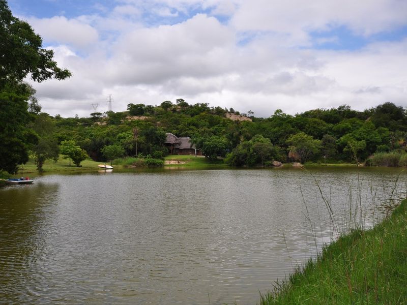 A scenic view of a tranquil farm dam surrounded by lush indigenous vegetation and rolling hills.