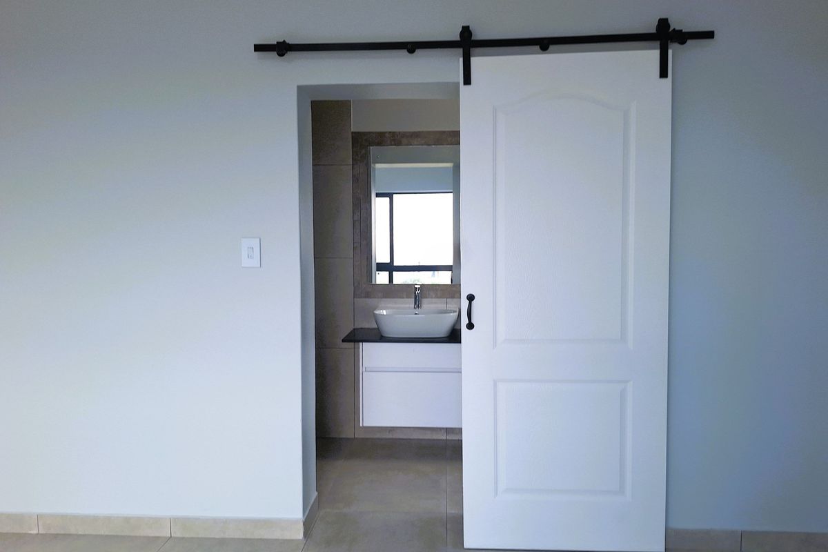 A modern bathroom featuring a vessel sink, vanity cabinet, and a wall-mounted mirror, accessed via a white sliding barn door.