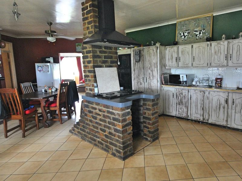 Open-plan kitchen featuring a central brick island with a built-in hob and extractor fan, complemented by rustic cabinetry and tiled flooring.