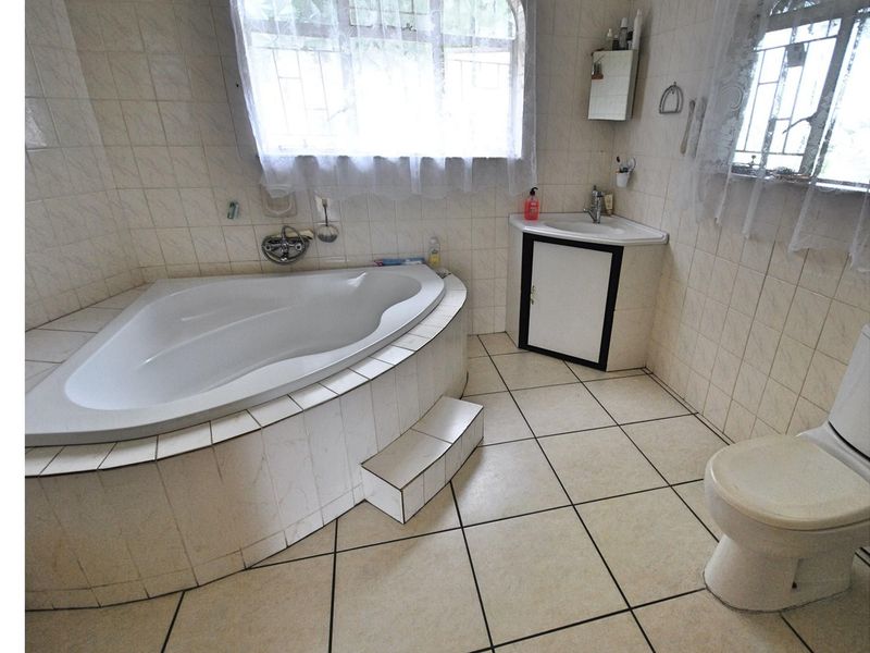 A functional bathroom featuring a corner bathtub, a corner vanity unit with integrated sink, and a standard toilet, finished with tiled walls and flooring.