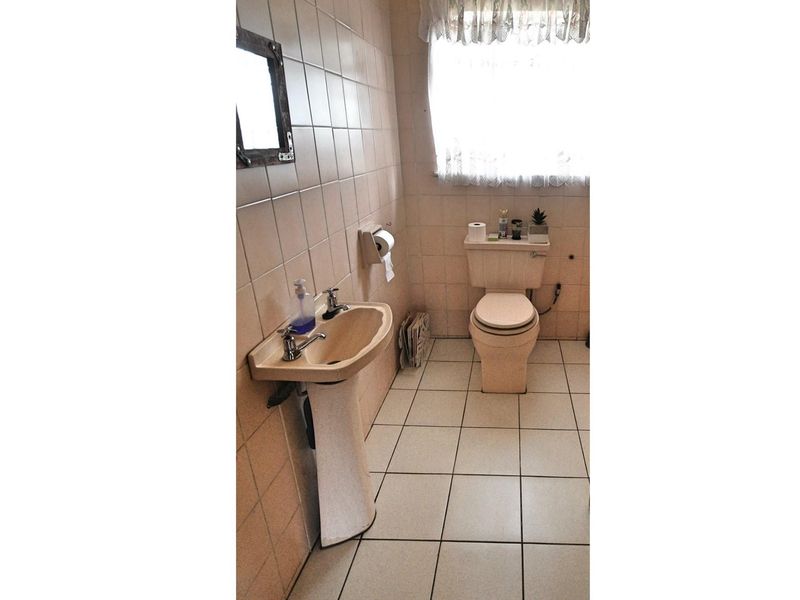 A dated bathroom featuring a pedestal basin and toilet with neutral wall and floor tiling.