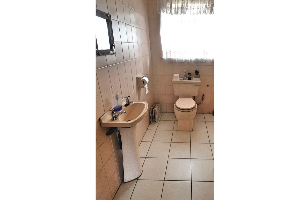 A dated bathroom featuring a pedestal basin and toilet with neutral wall and floor tiling.