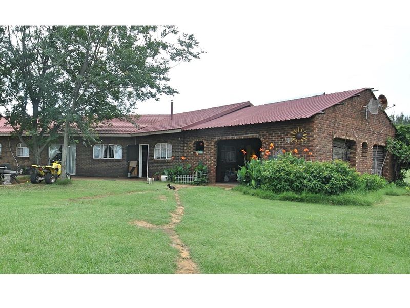 A rear view of a rustic face-brick farmhouse featuring a covered patio area, metal roof, and expansive surrounding lawn.