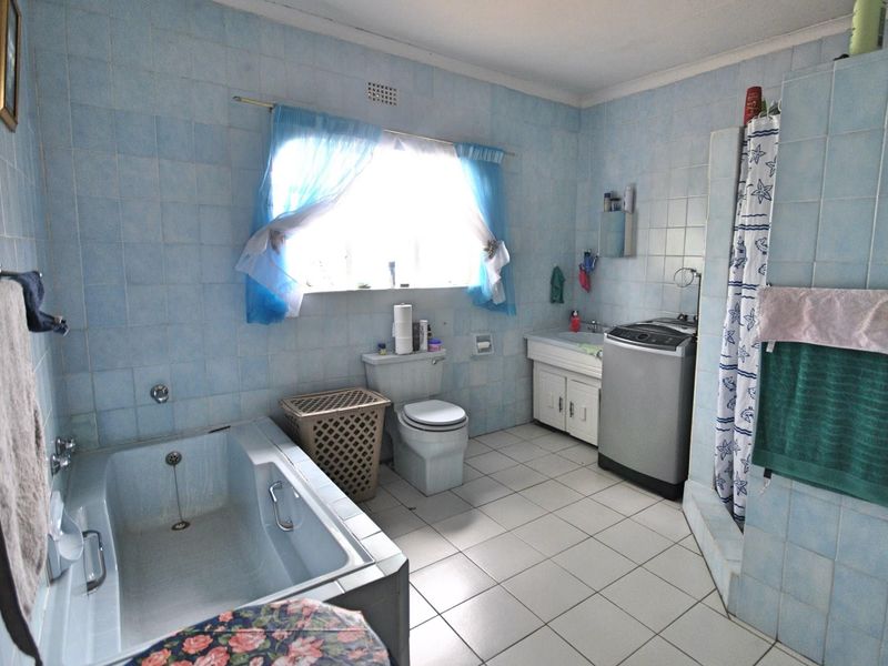A dated bathroom featuring blue wall tiles, a built-in bathtub, a toilet, a vanity basin, and space for a washing machine.