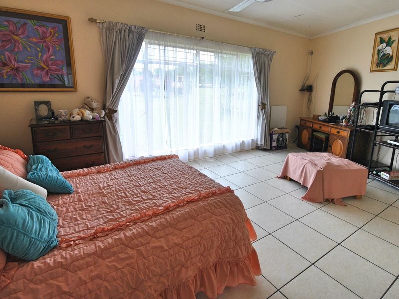 Spacious bedroom featuring large windows with natural light, tiled flooring, and a ceiling fan.