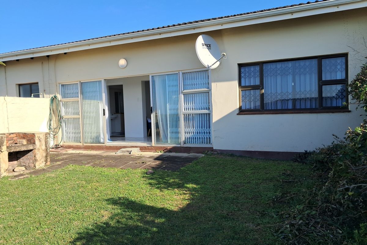 Rear view of the apartment featuring a paved patio area, built-in brick braai, sliding glass doors with security gates, and a private garden.