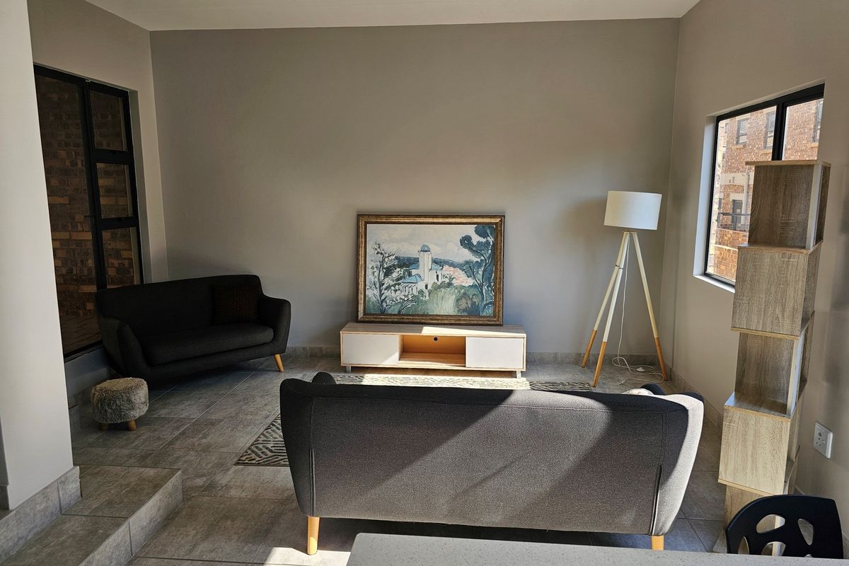 A bright and spacious living room featuring neutral tiled flooring, large windows, and a clean, modern aesthetic suitable for comfortable apartment living.