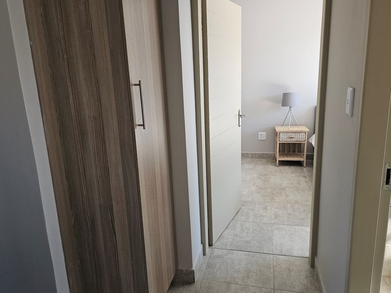 A view from a hallway looking into a bedroom, featuring tiled flooring and a built-in wooden cupboard.