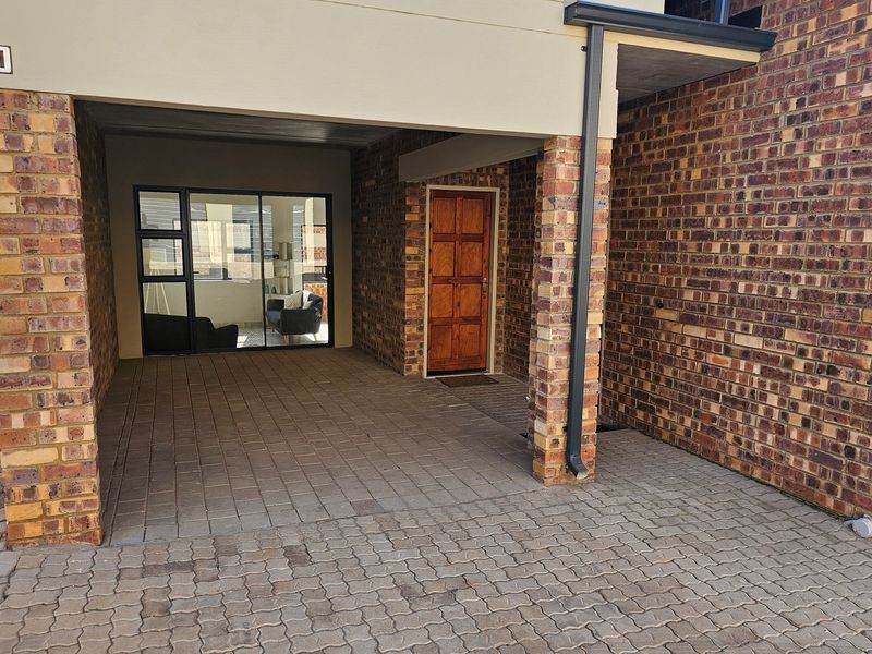 Covered entrance area featuring brick facade, paved flooring, and a solid timber front door with adjacent sliding glass door access.