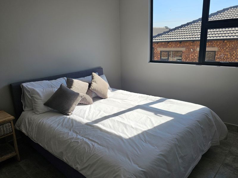 A bright and modern bedroom featuring tiled flooring, neutral walls, and a large window with black framing.