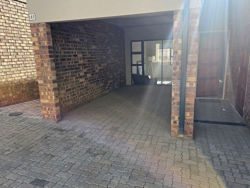 A covered carport area featuring exposed brick walls and paved flooring, providing direct access to the apartment entrance.