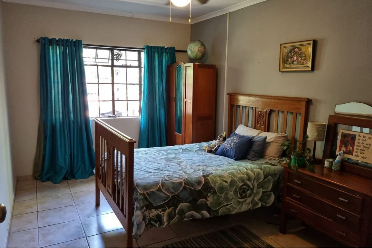 A functional bedroom featuring tiled flooring, a window with security bars, and neutral wall finishes.