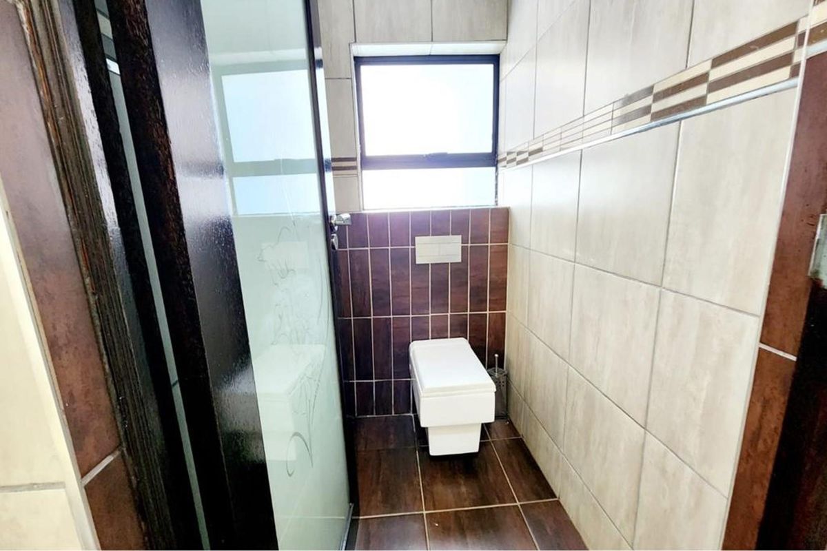 A compact bathroom featuring a wall-mounted toilet, dark wood-look floor tiles, and contrasting wall tiling with a window for natural light.