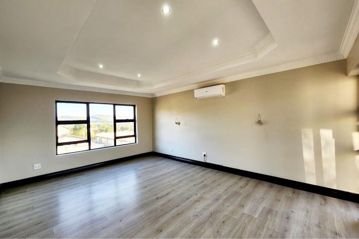Spacious bedroom featuring modern laminate flooring, recessed tray ceiling with downlights, wall-mounted air conditioning unit, and large windows providing natural light.