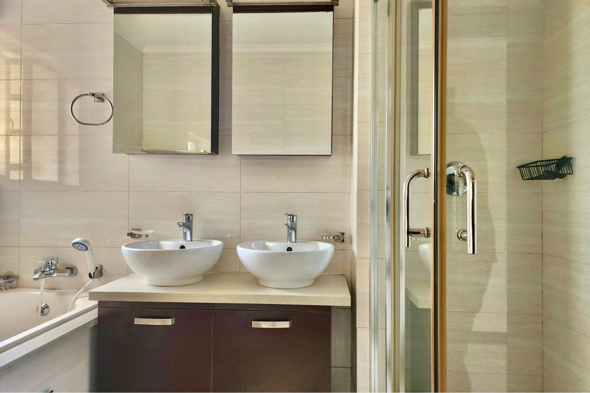 Modern bathroom featuring a double vanity with vessel sinks, medicine cabinets, a separate shower enclosure, and a bathtub with neutral wall tiling.