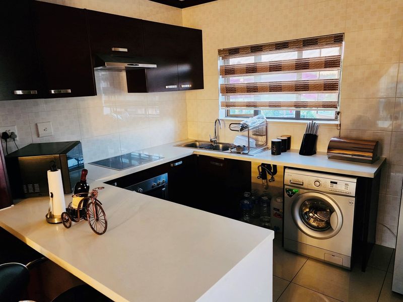 Compact kitchen featuring dark wood cabinetry, stone countertops, integrated appliances, and a breakfast bar, with tiled backsplash and functional layout.