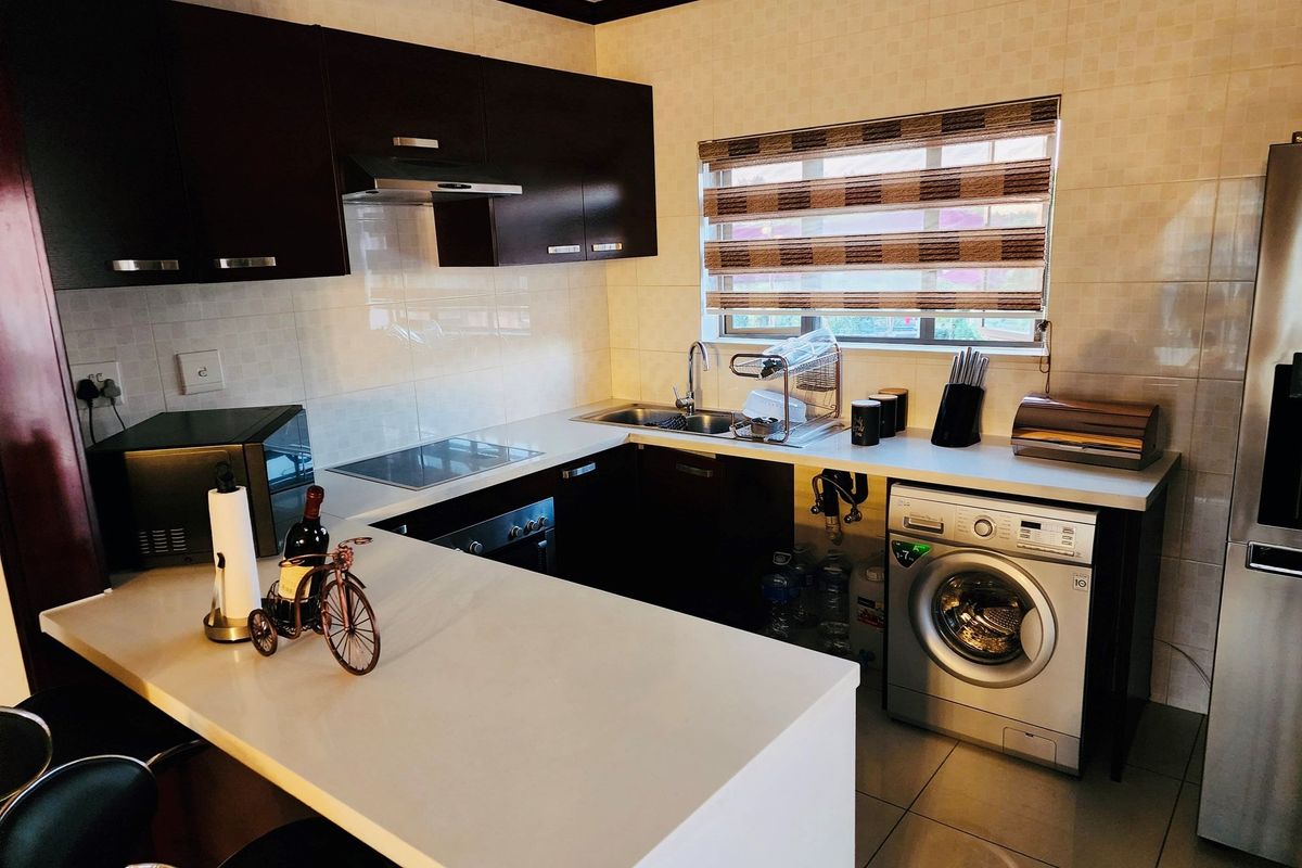 Compact kitchen featuring dark wood cabinetry, stone countertops, integrated appliances, and a breakfast bar, with tiled backsplash and functional layout.