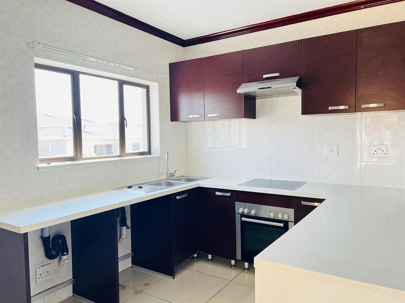 A functional kitchen featuring dark wood cabinetry, a built-in oven with hob, extractor fan, and tiled splashbacks, offering a clean and practical workspace.