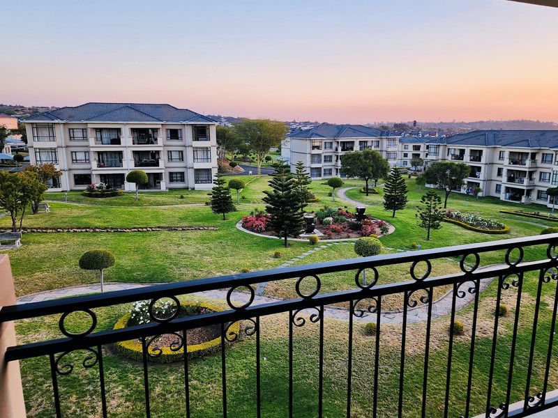 Elevated view from a balcony overlooking a well-maintained communal garden area and surrounding apartment complex buildings at sunset.