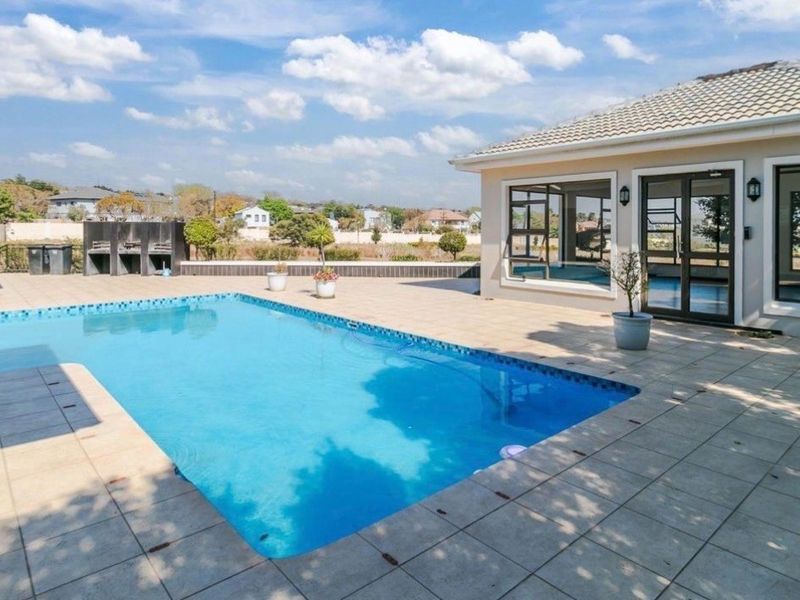 Spacious outdoor pool area featuring a large swimming pool, tiled patio, and a built-in braai, perfect for outdoor entertaining.