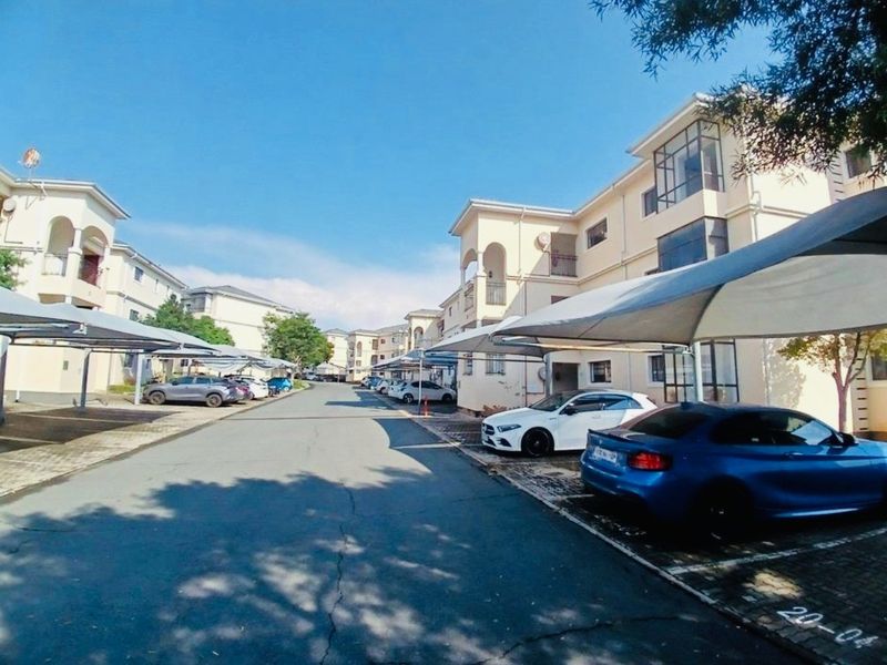 Exterior view of the apartment complex featuring paved parking bays with shade sail carports and an asphalt driveway.