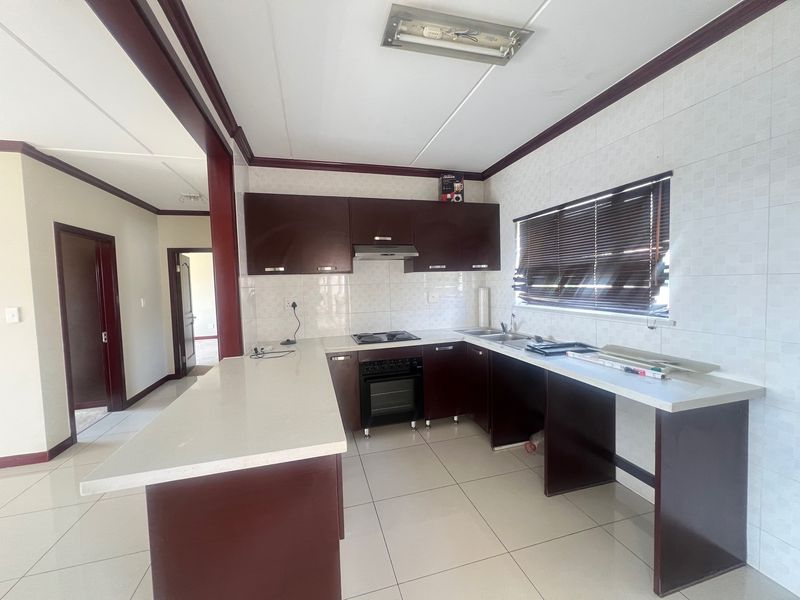 A functional kitchen featuring dark wood cabinetry, stone countertops, built-in oven, hob, and tiled finishes throughout. The space is clean and ready for personalization.