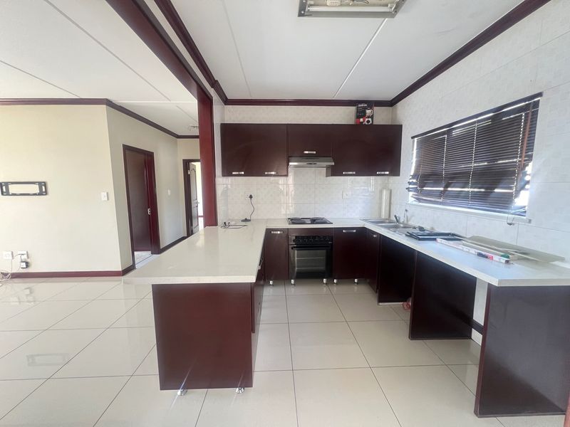 A spacious, open-plan kitchen featuring dark wood cabinetry, stone countertops, built-in oven, hob, and extractor fan, complemented by neutral tiled flooring.