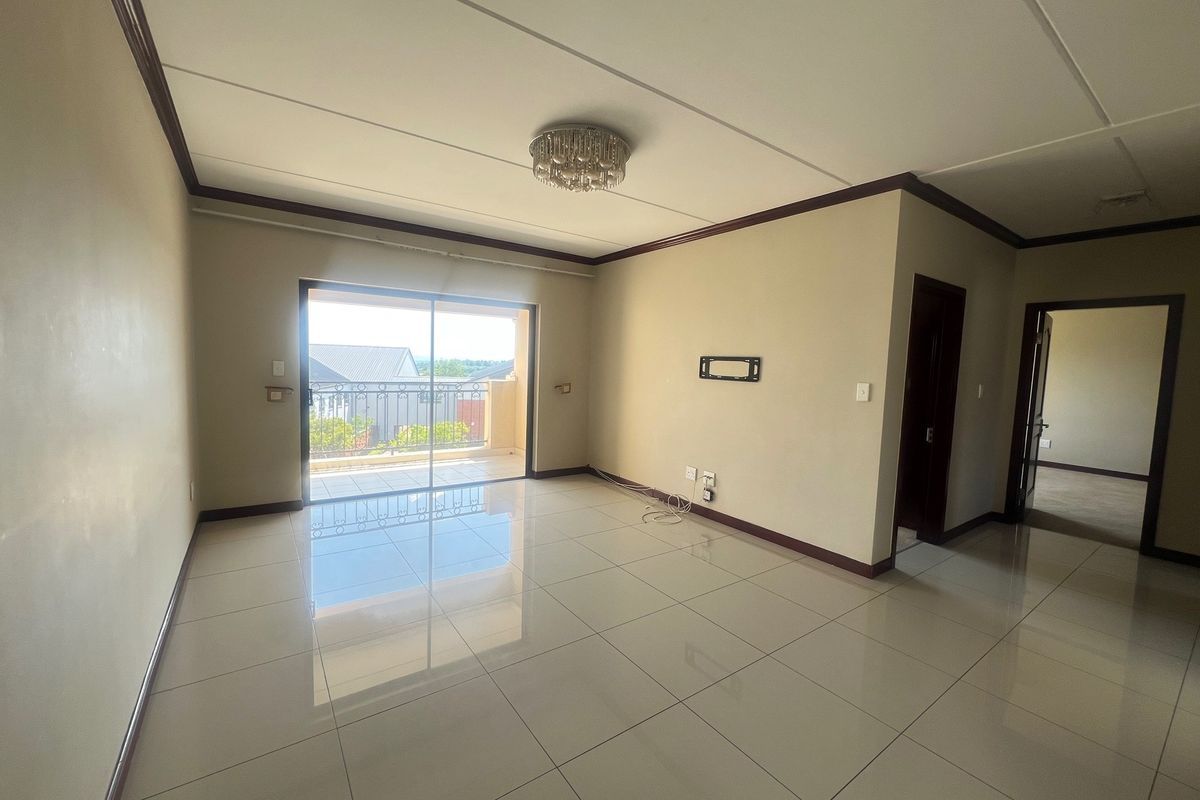 Spacious, empty living area featuring polished tile flooring, neutral walls, and a sliding glass door providing access to a private balcony.