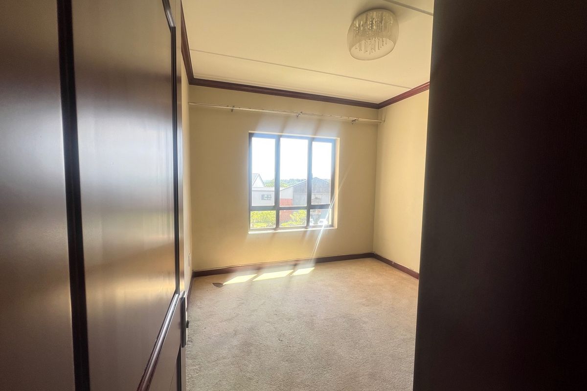 An empty bedroom featuring carpet flooring, crown molding, and a window providing natural light.