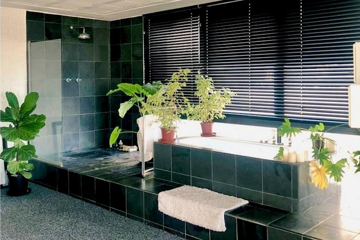 A spacious bathroom featuring a raised platform with a built-in bathtub and a separate walk-in shower, finished with dark slate-style tiling.