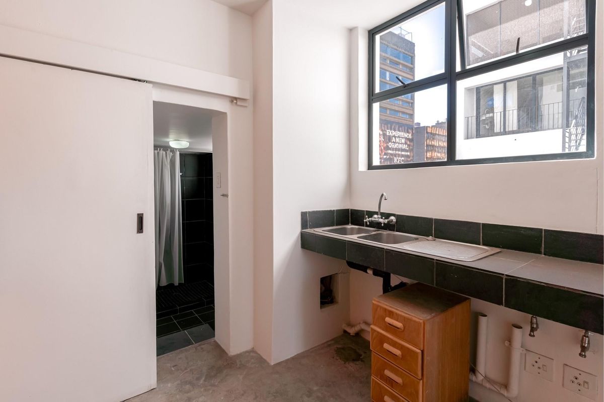 A functional utility or kitchen area featuring a double sink with tiled counter, large window, and direct access to an adjacent bathroom.