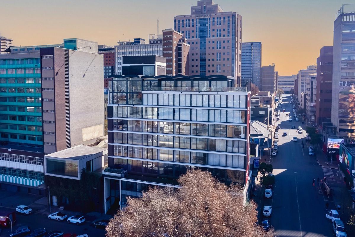 Aerial view of a modern multi-story apartment building featuring extensive glass facades and a prominent rooftop structure in an urban city setting.