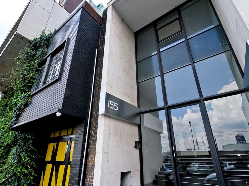 Modern apartment building entrance featuring a striking black brick facade, climbing greenery, and large floor-to-ceiling glass windows with contemporary architectural detailing.