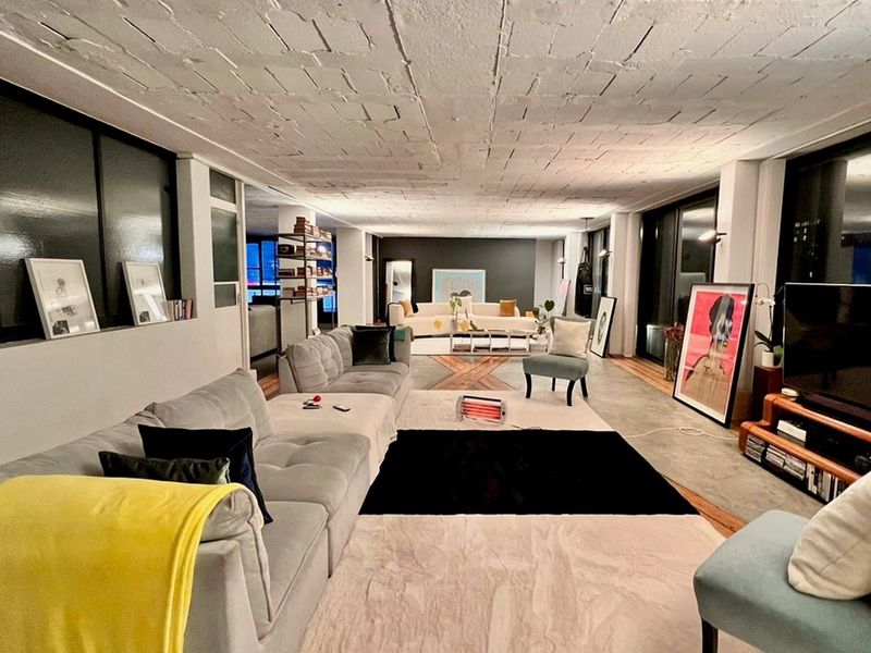 Spacious open-plan living area featuring industrial-style exposed concrete ceilings, polished concrete flooring, and large windows providing ample natural light.