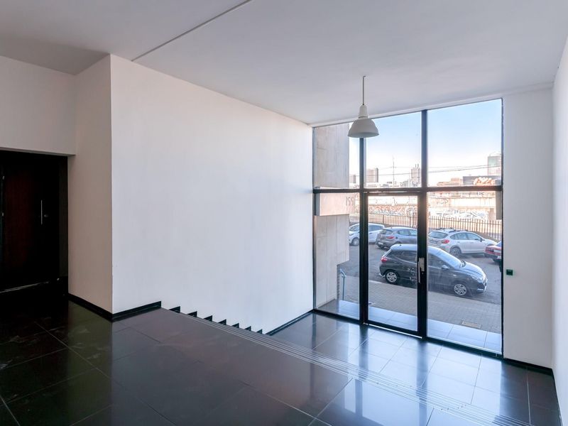 A bright and spacious apartment entrance foyer featuring large floor-to-ceiling windows, dark tiled flooring, and a modern minimalist aesthetic.