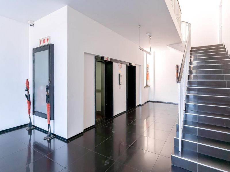 A modern apartment building lobby featuring a sleek staircase with metal railings, polished dark floor tiles, and elevator access.